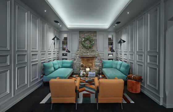 Lobby mit Kamin Moderner Aufenthaltsraum mit Steinkamin, zwei türkisfarbenen Sofas und zwei braunen Sesseln vor grauer Wandtäfelung.
