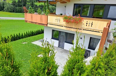Ferienwohnung Widmann Jochberg Modernes Alpenhaus mit Holzbalon, Terrasse und Gartenanlage vor grüner Bergkulisse.