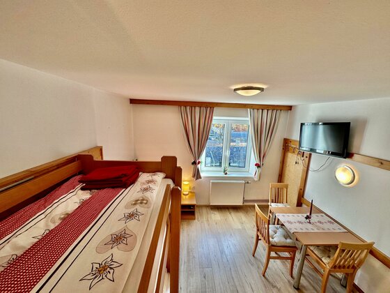 Innenansicht eines Zimmers mit Holz-Etagenbett, Esstisch und Fernseher.