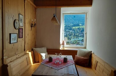 Rustikale Sitzecke aus Holz mit Esstisch und Blick aus dem Fenster auf eine Berglandschaft.