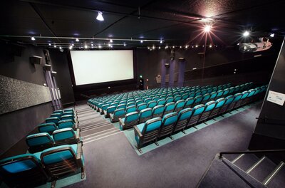 Ein modernes Kino mit blauen Sitzen und einem großen Bildschirm. Der Raum ist bereit für die nächste Filmvorführung.