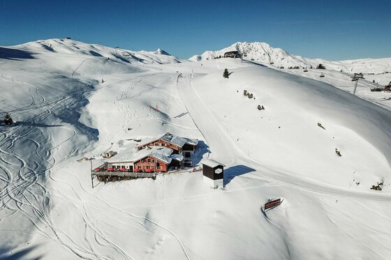 Vogelperspektive auf das Berggasthaus Resterhöhe inmitten einer verschneiten Gebirgslandschaft mit Skipisten.