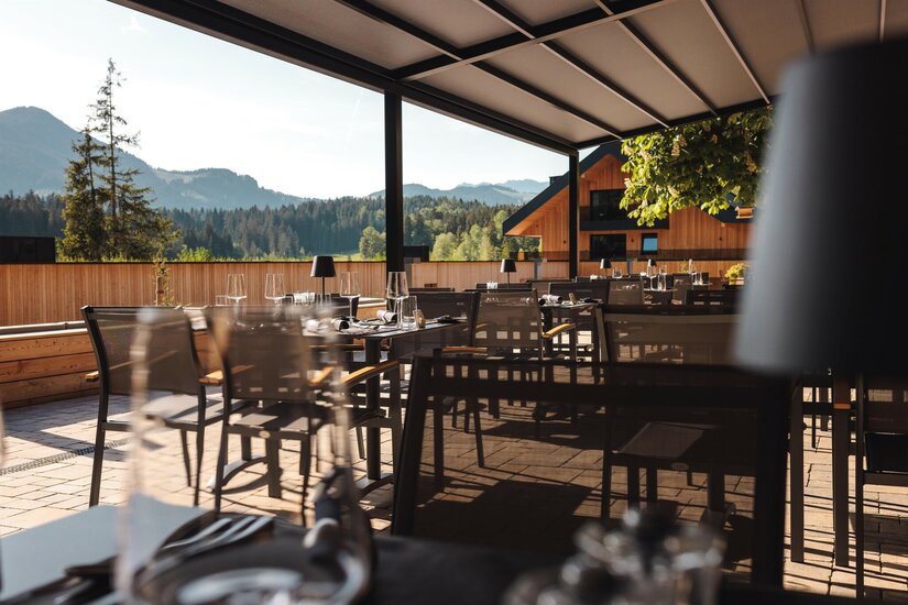 Terrasse Alpenhotel Kitzbühel Überdachte Restaurantterrasse mit gedeckten Tischen, Blick auf Nadelwälder und Berge.
