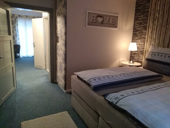 Schlafzimmer der Kitzbüheler Suite Ein Doppelbett in einem Schlafzimmer mit Blick durch eine offene Tür in einen weiteren Raum.