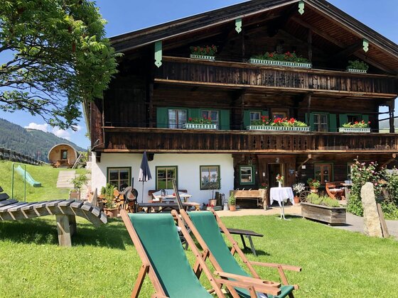 Alpines Holzhaus mit Garten Traditionelles Holzhaus mit Balkonen, Blumenkästen und Liegestühlen auf einer grünen Wiese.