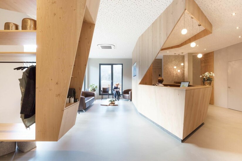 Empfangsbereich Gynova Moderner Empfangsbereich mit hellem Holz-Tresen, Sitzgelegenheiten und Garderobe.