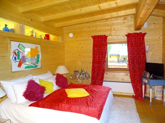 Schlafzimmer Golfweg 10 Schlafzimmer in einer Holzhütte mit Doppelbett, roten Vorhängen und einem bunten Wandbild.