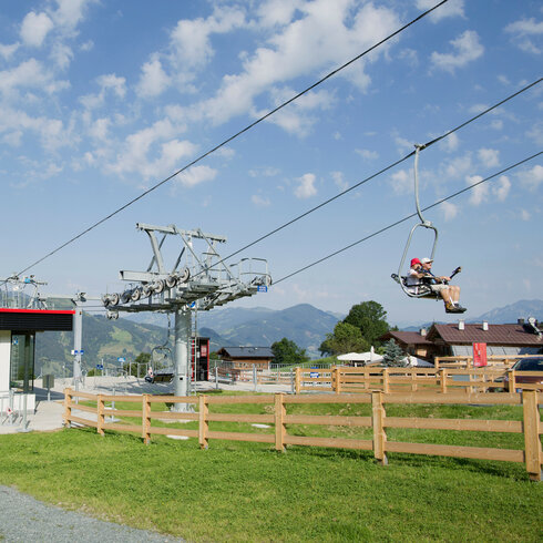 Eine Seilbahnstation mit einem modernen Gebäude und einem Fahrstuhl, der über grüne Wiesen in die Berge führt.