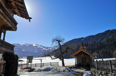 Hennleiten im Winter Alpines Holzhaus und kleine Kapelle vor verschneiter Berglandschaft unter blauem Himmel.