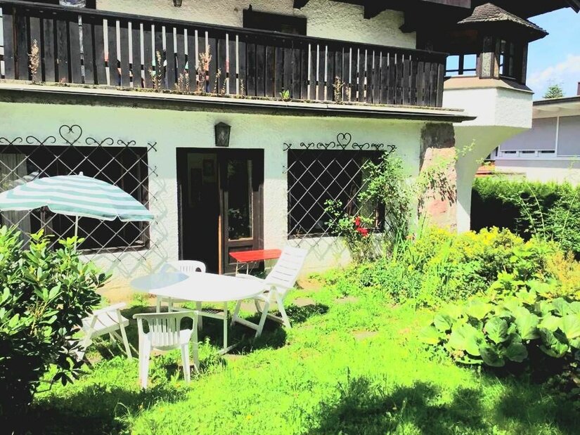 Terrasse und Garten der Stadtvilla Gretl Garten mit weißen Kunststoffmöbeln, Sonnenschirm und einer Terrasse vor einem Haus mit Holzbalkon.