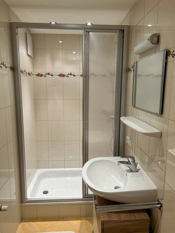 Badezimmer Ein modernes Badezimmer mit einer Dusche, einem Waschbecken mit einem Spiegel und WC. Die Wände sind gefliest und neutral gehalten.