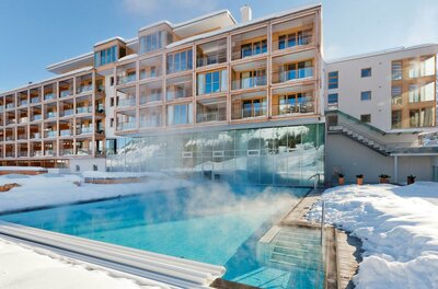 Winter-Außenpool Kempinski Hotel Dampfender Außenpool vor einem modernen Hotelgebäude in verschneiter Landschaft.