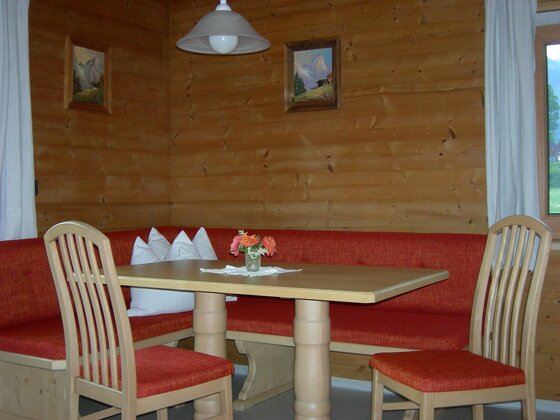 Bergschmied Essecke Essecke mit Holztisch, roter Eckbank und zwei Stühlen in einer holzgetäfelten Stube.