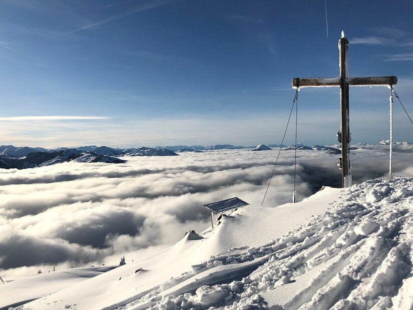 Gipfelkreuz am Hochetzkogel Gipfelkreuz auf dem verschneiten Hochetzkogel über einer geschlossenen Wolkendecke unter blauem Himmel.