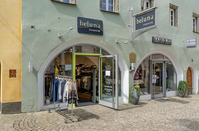 Außenansicht des Modegeschäfts Beluna Fashion mit zwei Rundbogen-Eingängen und Kleiderständer auf Kopfsteinpflaster.