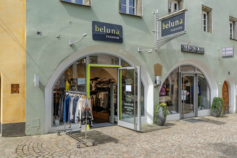 Beluna Fashion Ladengeschäft Außenansicht des Modegeschäfts Beluna Fashion mit zwei Rundbogen-Eingängen und Kleiderständer auf Kopfsteinpflaster.
