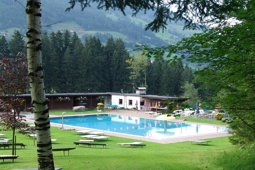 Waldschwimmbad Jochberg Freibad mit blauem Becken, Liegewiese und Holzgebäuden vor bewaldetem Berghang.