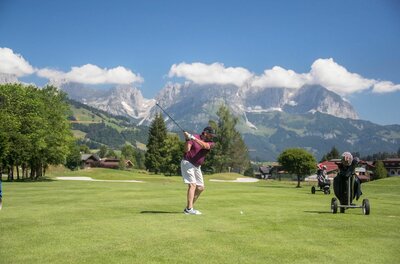Golfclub Kitzbühel Schwarzsee Reith Ein Mann beim Golfschwung auf einem grünen Golfplatz vor einer alpinen Bergkulisse.