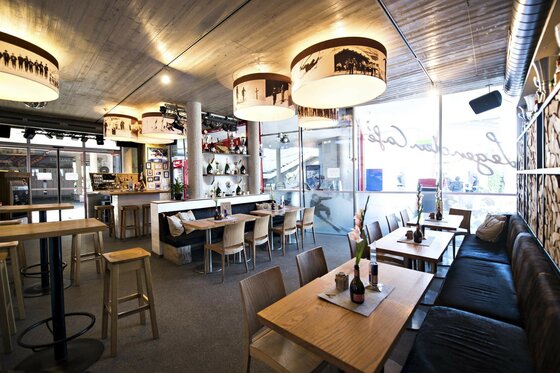 Innenraum Legenden Café Innenansicht eines Cafés mit Holztischen, Sitzbänken und runden Hängelampen mit historischen Skimotiven.