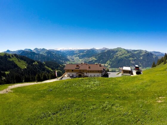 Alpengasthof Bichlalm Panorama Alpengasthof auf einer grünen Bergwiese vor einem weiten Gebirgspanorama unter blauem Himmel.