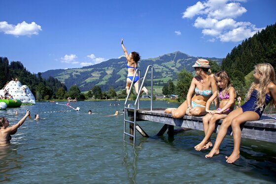 Salvenaland @ Region Hohe Salve - Thomas Trinkl Ein Schwimmbad mit vielen Kindern und Familien am Wasser. Im Hintergrund sind grüne Berge und ein blauer Himmel zu sehen.