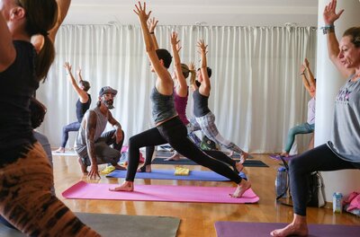 Eine Gruppe von Menschen übt Yoga in einem hellen Raum. Die Teilnehmer sind in verschiedenen Yoga-Posen und konzentrieren sich auf ihre Bewegungen.