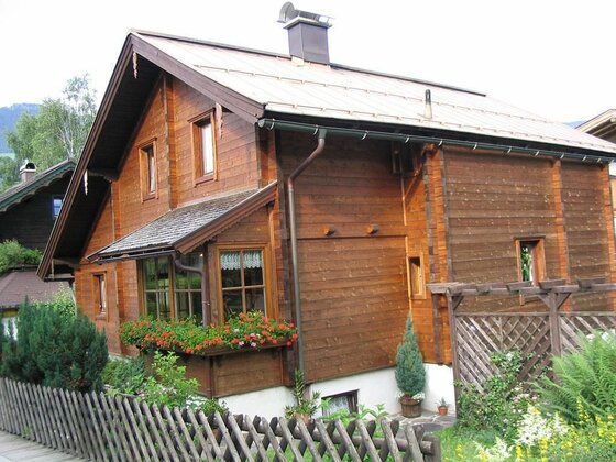 Zweistöckiges Holzhaus mit Satteldach, Blumenkästen und Holzzaun im Vordergrund.