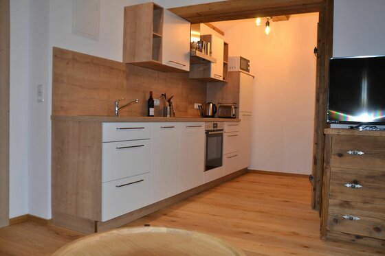 Küche im Brandhof Moderne Küchenzeile mit weißen Fronten, Holz-Arbeitsplatte und eingebauten Elektrogeräten in einer Ferienwohnung.