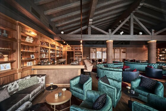 Innenansicht einer Bar mit Holztheke, grünen Samtsesseln und offenem Dachstuhl aus dunklem Holz.