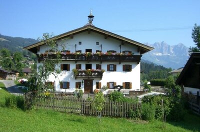 Seiwaldhof Ein traditionelles alpenländisches Haus mit Balkon und vielen Blumen. Im Hintergrund sind die Berge und ein blauer Himmel sichtbar.