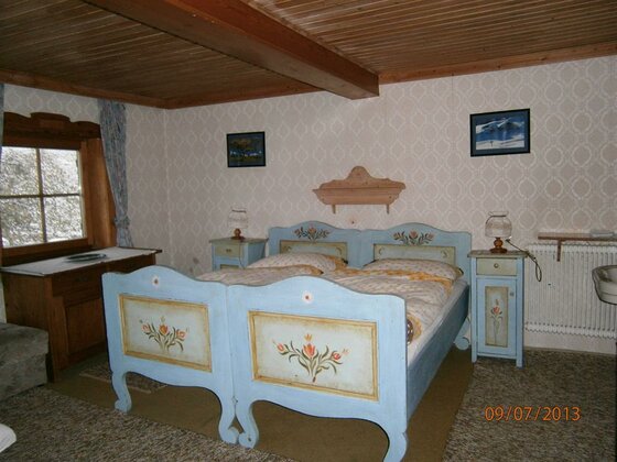Rustikales Schlafzimmer mit zwei hellblauen Holzbetten mit Blumenmalerei und Holzdecke.