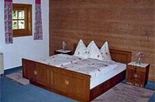 Rustikales Doppelbett aus Holz vor einer Holzwand mit zwei Nachttischen und einem kleinen Fenster.