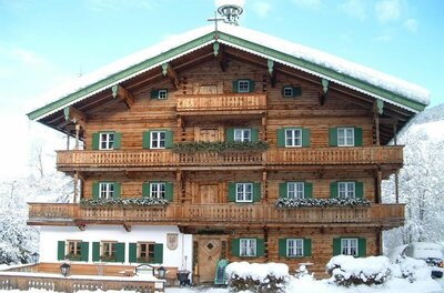 Hallerwirt Homes im Winter Mehrstöckiges Holzhaus im alpinen Stil mit grünen Fensterläden und schneebedecktem Dach im Winter.