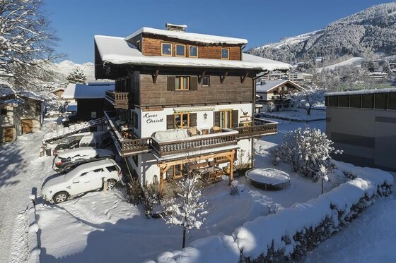 Mehrstöckiges Alpenhaus mit Holzfassade und schneebedecktem Dach in einer Winterlandschaft.