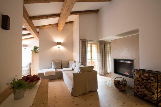 Wohnraum Hallerwirt Homes Moderner Wohnraum mit Ecksofa, Holzbalkendecke, Kamin und Brennholzregal.