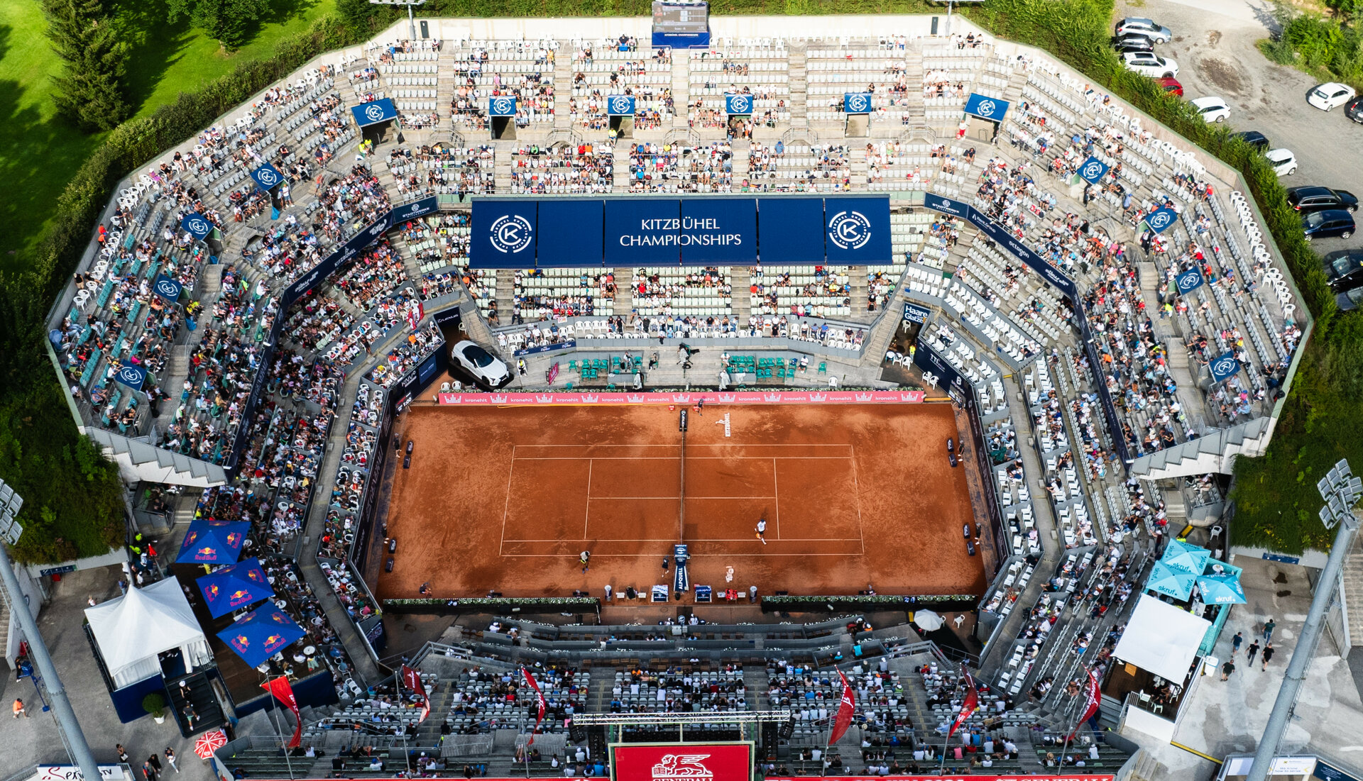 Eine Luftaufnahme des Tennisstadions bei den Kitzbüheler Meisterschaften, umgeben von Zuschauern und grüner Landschaft.