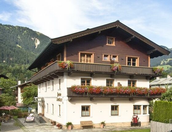 Pension Schmidinger Außenansicht Dreistöckiges alpines Gästehaus mit Blumenbalkonen vor bewaldeten Bergen.