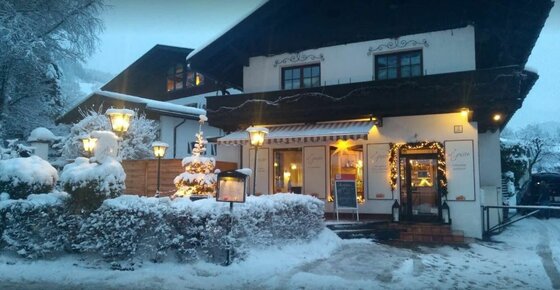 Restaurant Il Gusto im Winter Ein verschneites Gasthaus bei Dämmerung mit beleuchteten Fenstern und Weihnachtsdekoration.