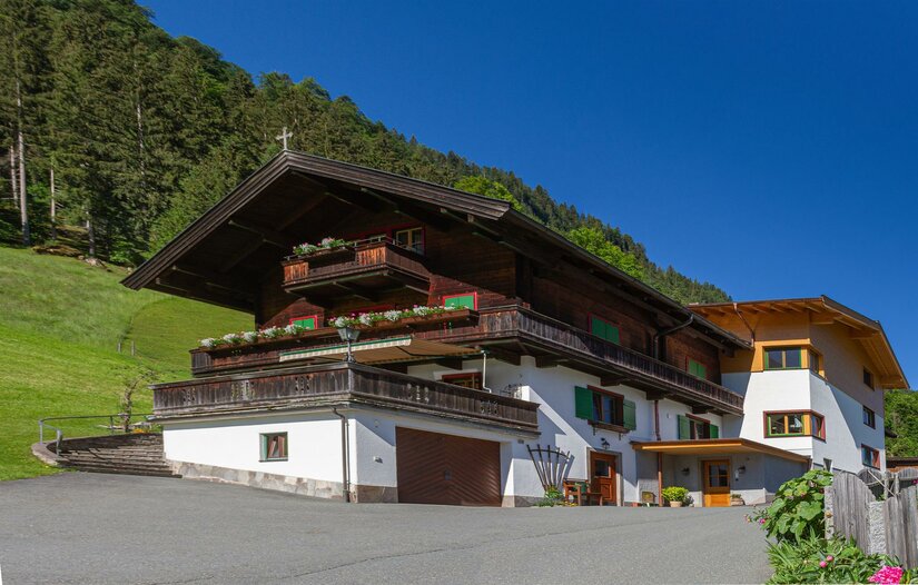 Ferienhof Oberstaudach Alpiner Ferienhof mit dunkler Holzfassade, Balkonen und weißem Erdgeschoss vor bewaldetem Hang.