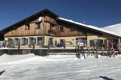 Steinbergkogel Hütte im Winter Berghütte aus Holz und Stein im Schnee mit Skiern im Vordergrund unter blauem Himmel.