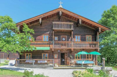 Ein charmantes Holzhaus im alpinen Stil mit einem schönen Balkon. Der Garten ist grün und einladend, ideal für entspannte Tage im Freien.