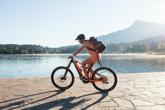 Mountainbiken am Schwarzsee Eine Mountainbikerin fährt auf einem gepflasterten Weg an einem See vor einer Bergkulisse.