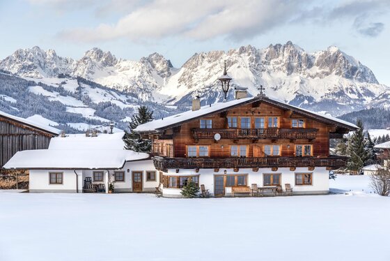 Außenansicht Winter Ferienwohnung Neuhaus Alpines Holzhaus mit schneebedecktem Dach vor einem verschneiten Gebirgspanorama.