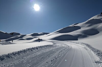 Präparierter Winterwanderweg in einer verschneiten Hügellandschaft unter blauem Himmel mit Sonnenschein.