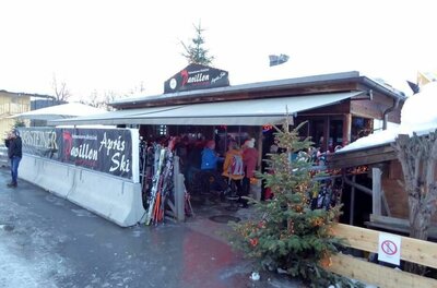 Hahnenkamm Pavillon Außenansicht des Hahnenkamm Pavillons mit Skifahrern und abgestellten Skiern unter einer Markise.