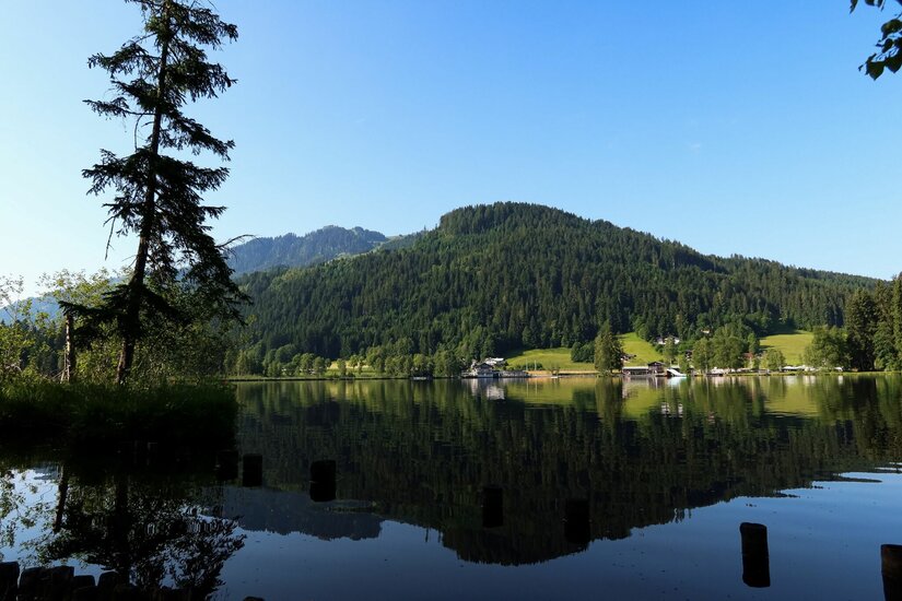 Schwarzsee Runde Blick über einen ruhigen See auf bewaldete Berge unter blauem Himmel mit Spiegelung im Wasser.