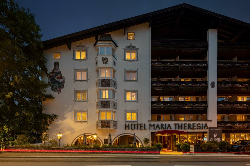 Beleuchtete Außenansicht des Hotel Maria Theresia bei Dämmerung mit Erker und Holzbalkonen.