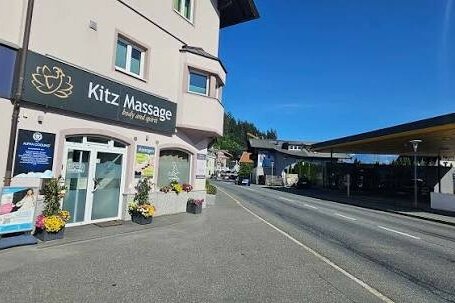Außenansicht des Kitz Massage Studios an einer befahrenen Straße neben einer Tankstelle unter blauem Himmel.