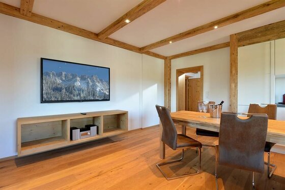 Moderner Wohnraum mit Holzbalkendecke, Esstisch, Stühlen und einem Fernseher an der Wand.