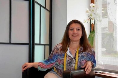 Ana's Schneiderei Eine Frau mit Maßband um den Hals sitzt in einem Raum neben einer Orchidee.